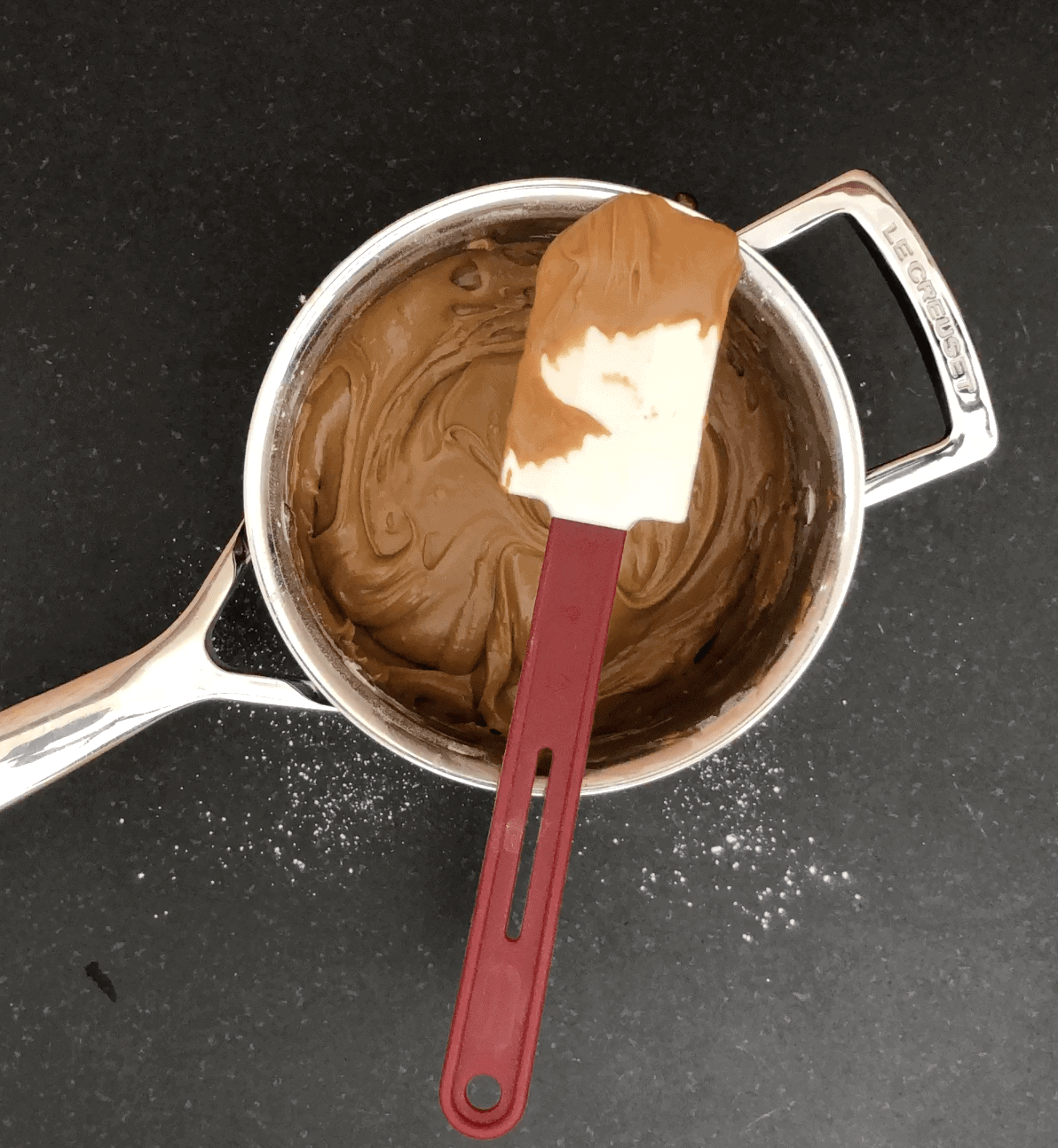 Light brown icing in a sauce pan with a white and red spatula