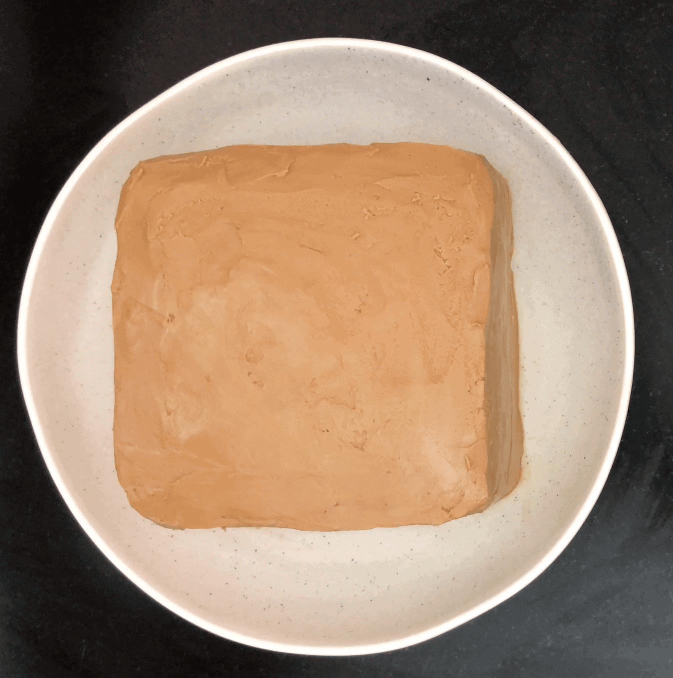 Square cake with light brown icing on a beige plate