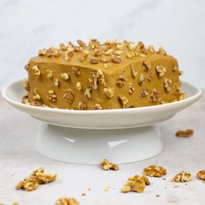Square cake on a white cake stand with golden brown icing decorated with walnut pieces