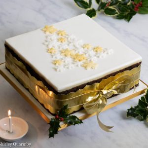Square xmas cake wrapped in gold ribbon with xmas tree decoration on top